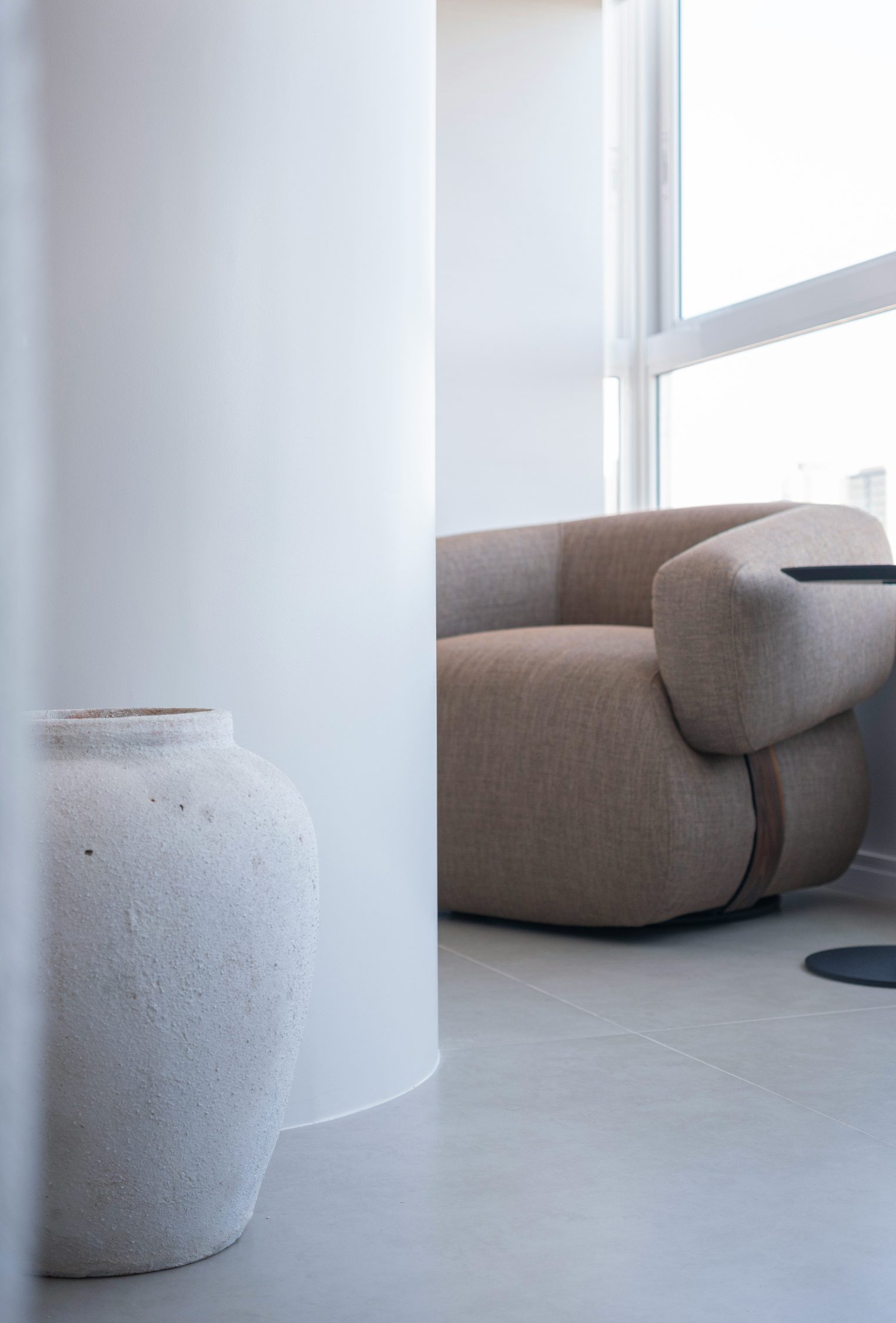 The Arc Lounge Chair: a rounded armchair in warm taupe beside a bright window