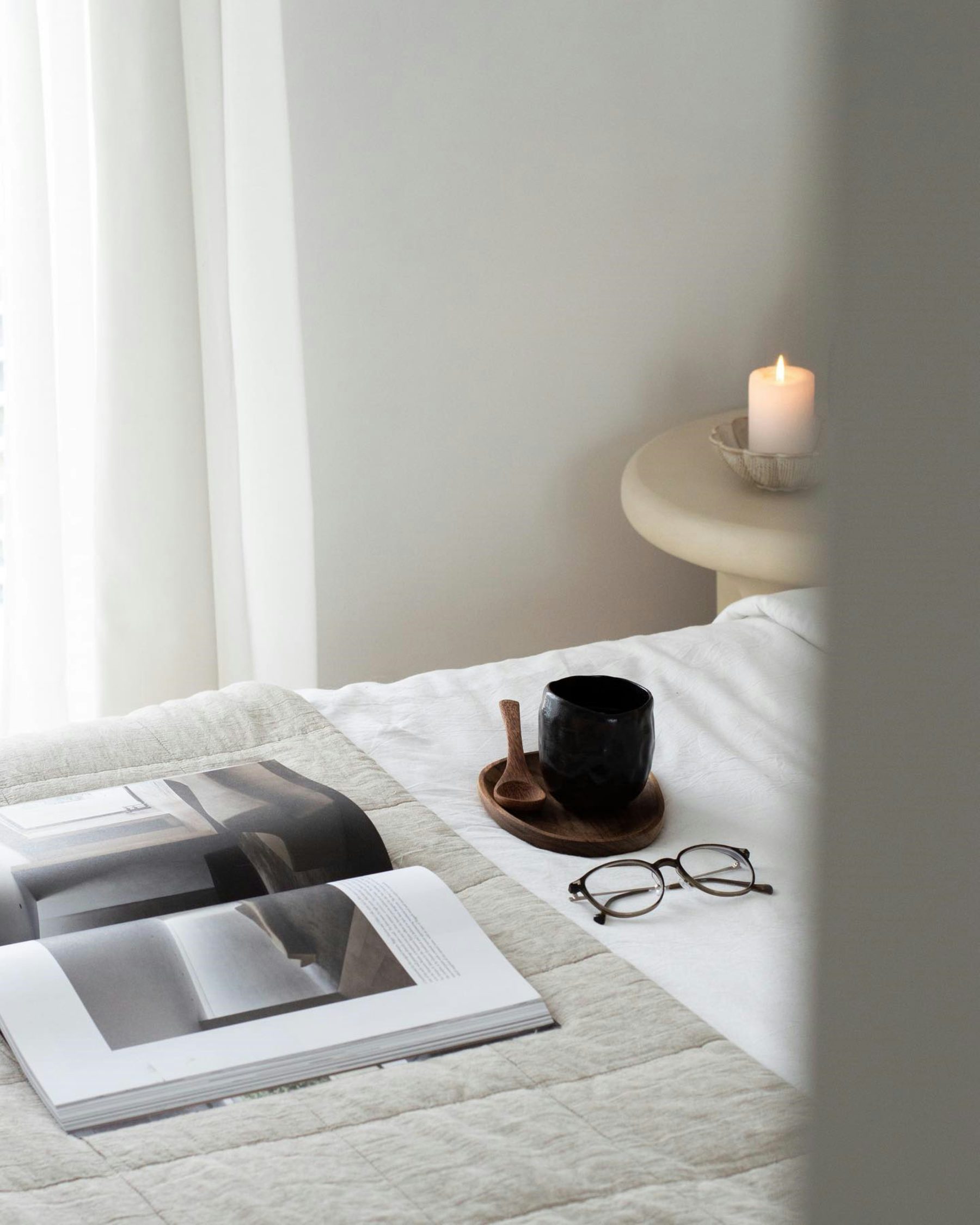 Soft linen bedding with a candle, a coffee cup and an open book in morning light